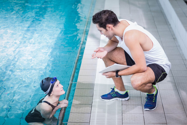 Fit trainer talking to swimmer in leisure center